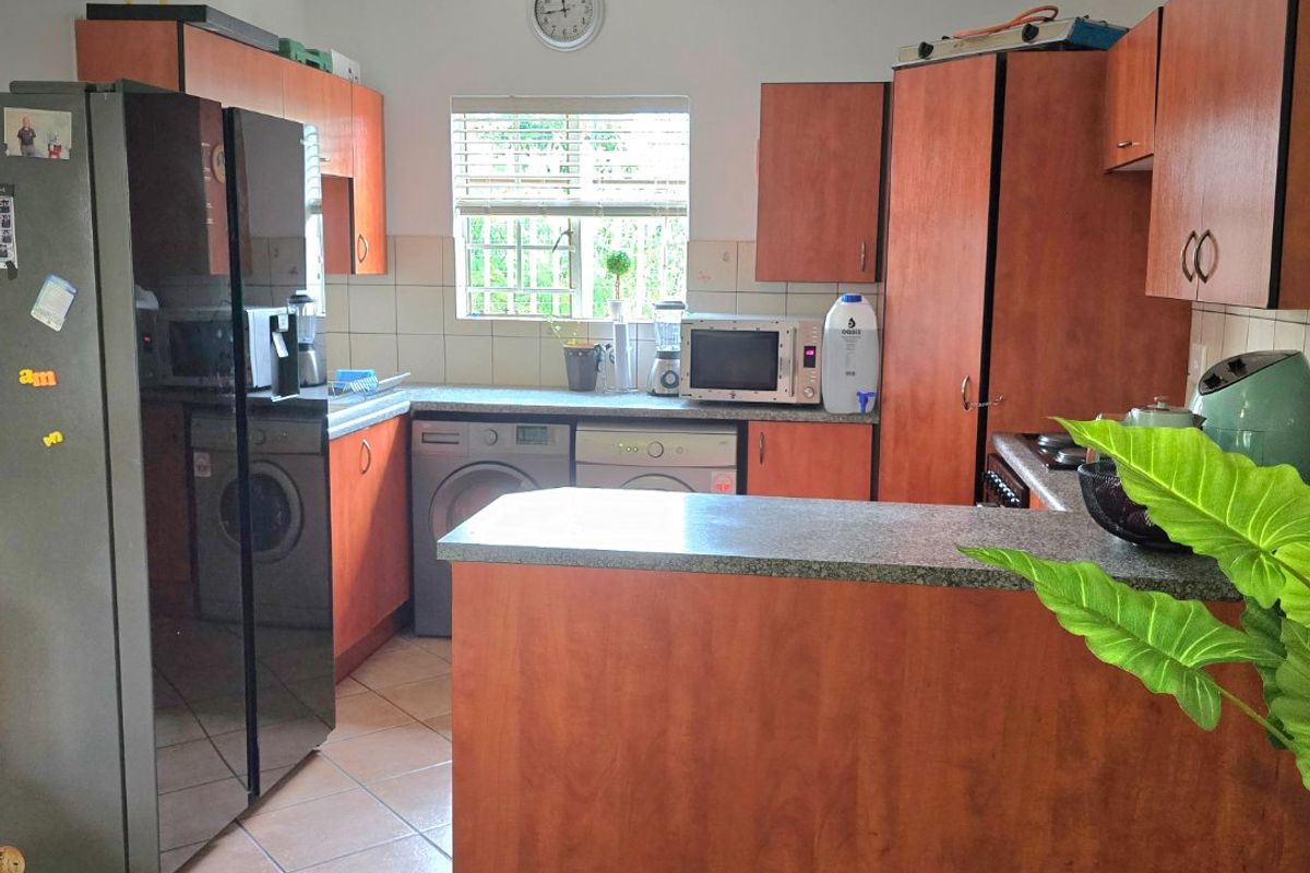 A functional kitchen featuring laminate cabinetry, stone-look countertops, tiled flooring, and integrated laundry appliance connections, offering a practical layout for daily use.