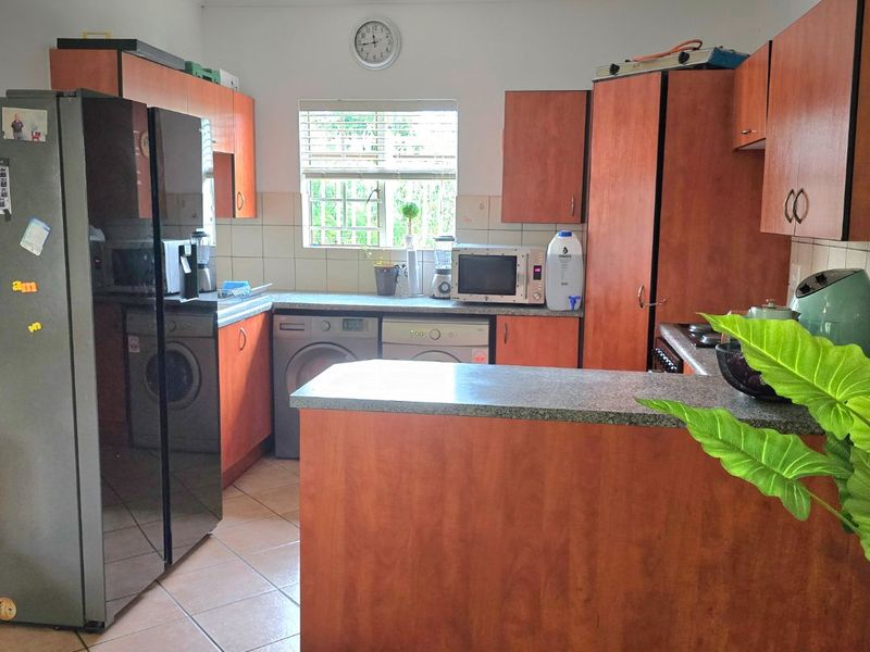 A functional kitchen featuring laminate cabinetry, stone-look countertops, tiled flooring, and integrated laundry appliance connections, offering a practical layout for daily use.