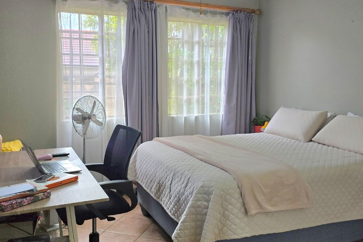 A functional bedroom featuring tiled flooring, a ceiling fan, and large windows that provide natural light.