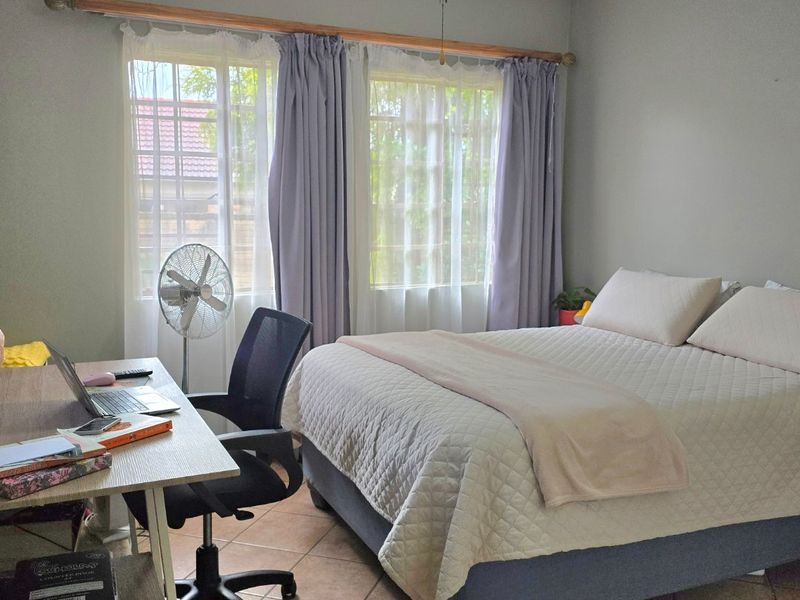 A functional bedroom featuring tiled flooring, a ceiling fan, and large windows that provide natural light.