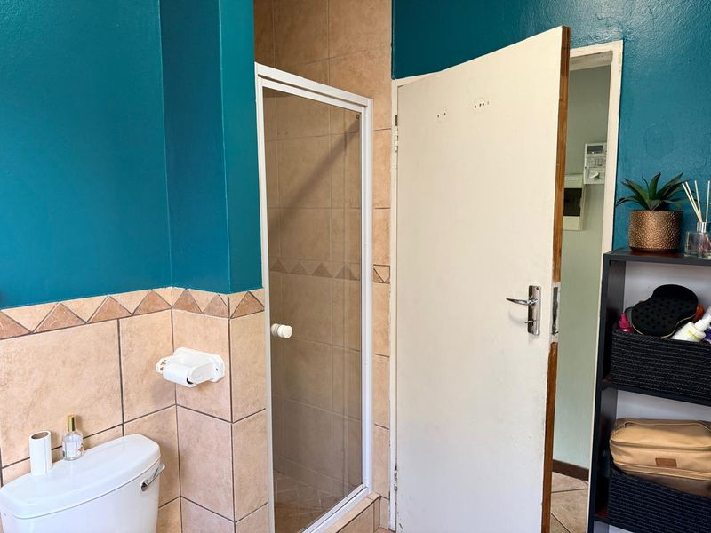 A functional bathroom featuring a shower enclosure, toilet, and tiled finishes. The space shows signs of wear on the door and requires cosmetic updates.