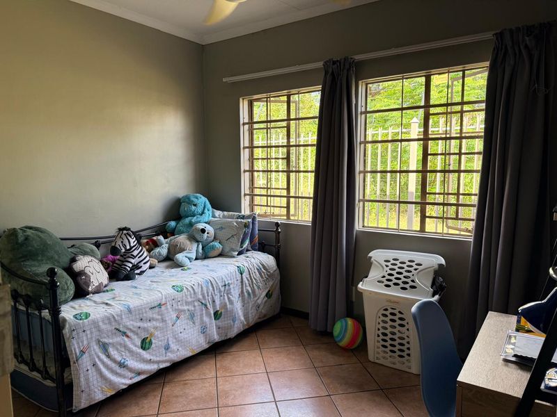 A bedroom featuring tiled flooring, a ceiling fan, and windows fitted with security bars, providing natural light and ventilation.