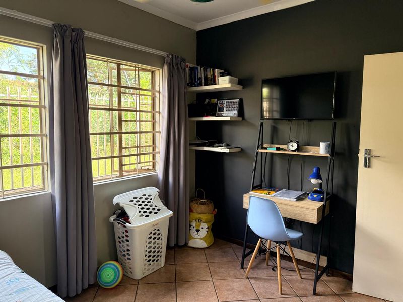 A bedroom featuring tiled flooring, built-in wall shelving, and large windows fitted with security burglar bars.