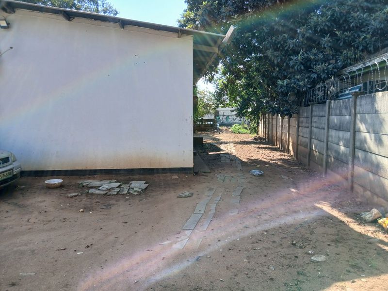 A view of the rear exterior area featuring a precast concrete boundary wall with razor wire and an unpaved ground surface.