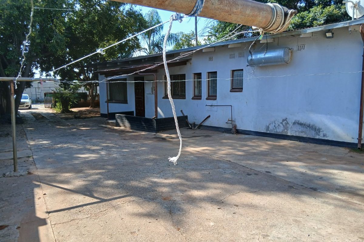 Rear exterior view of the property featuring a concrete driveway, external geyser, and security bars on windows, showing signs of wear and maintenance needs.
