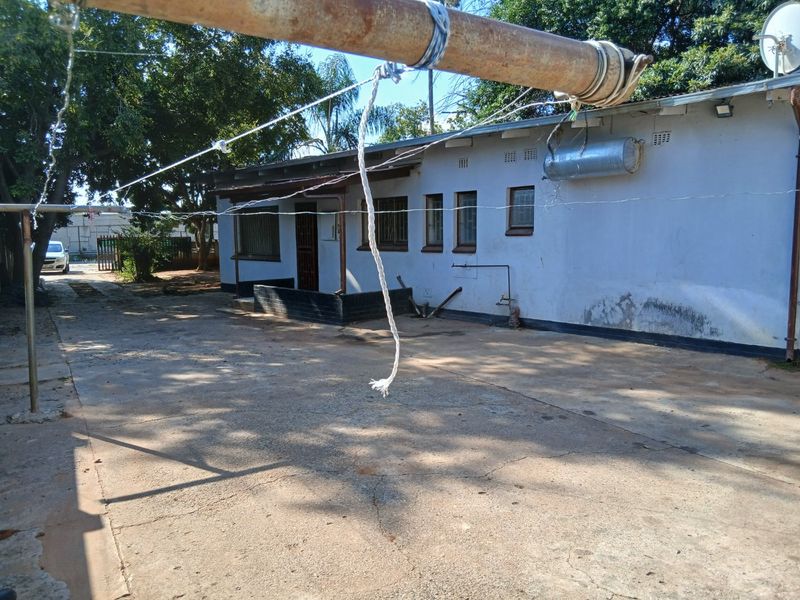 Rear exterior view of the property featuring a concrete driveway, external geyser, and security bars on windows, showing signs of wear and maintenance needs.