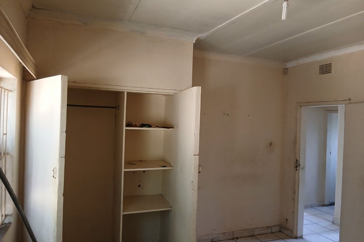An empty bedroom featuring tiled flooring and a built-in wardrobe, requiring cosmetic updates to the walls and finishes.