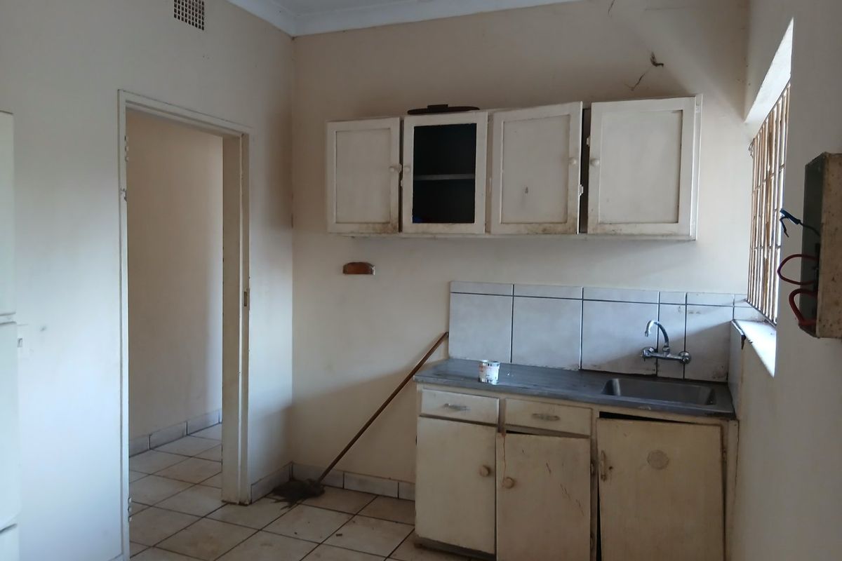 A dated, empty kitchen featuring original cabinetry, a single sink, and tiled finishes, requiring significant renovation and repair to the ceiling and walls.