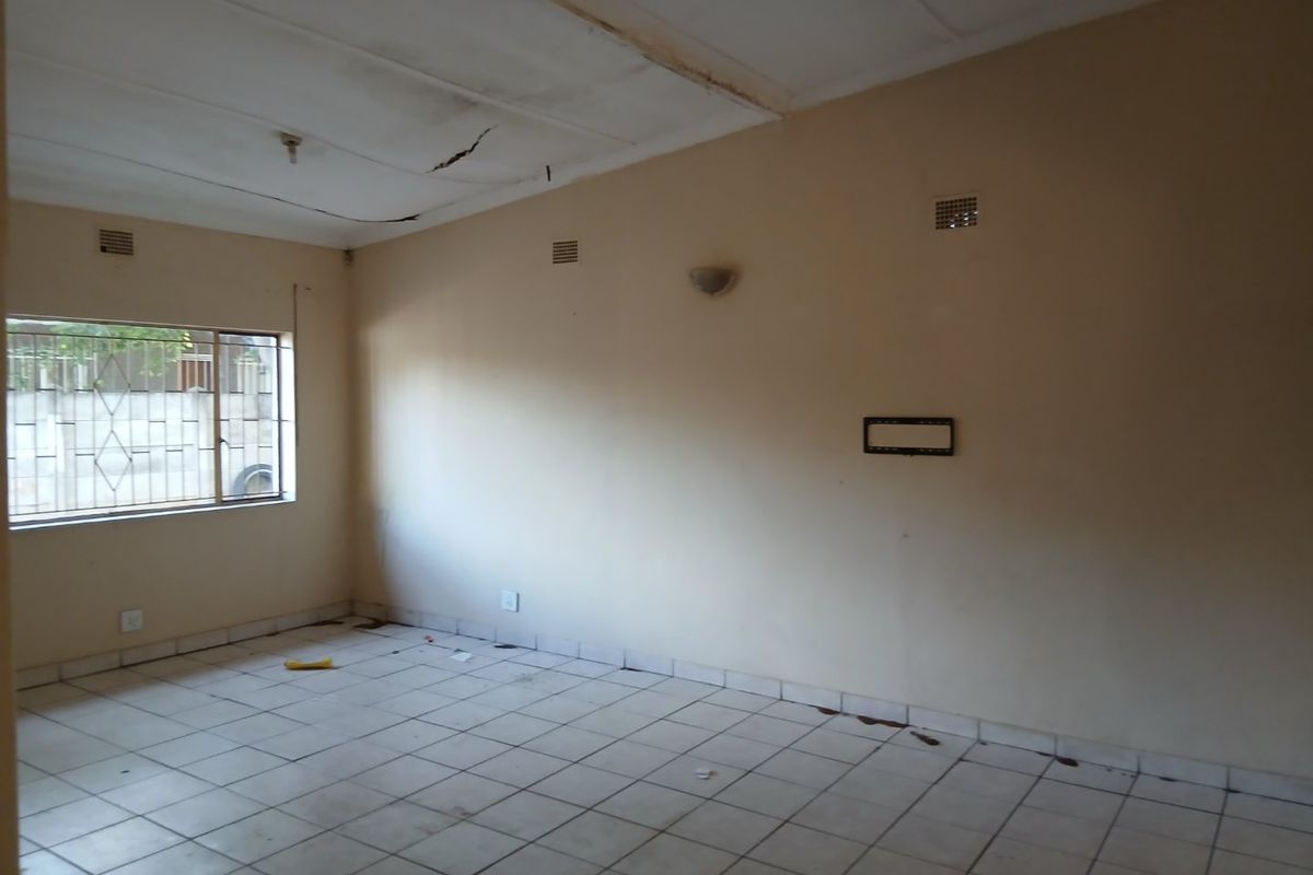 An empty living room featuring tiled flooring, security bars on the window, and a ceiling requiring repair.