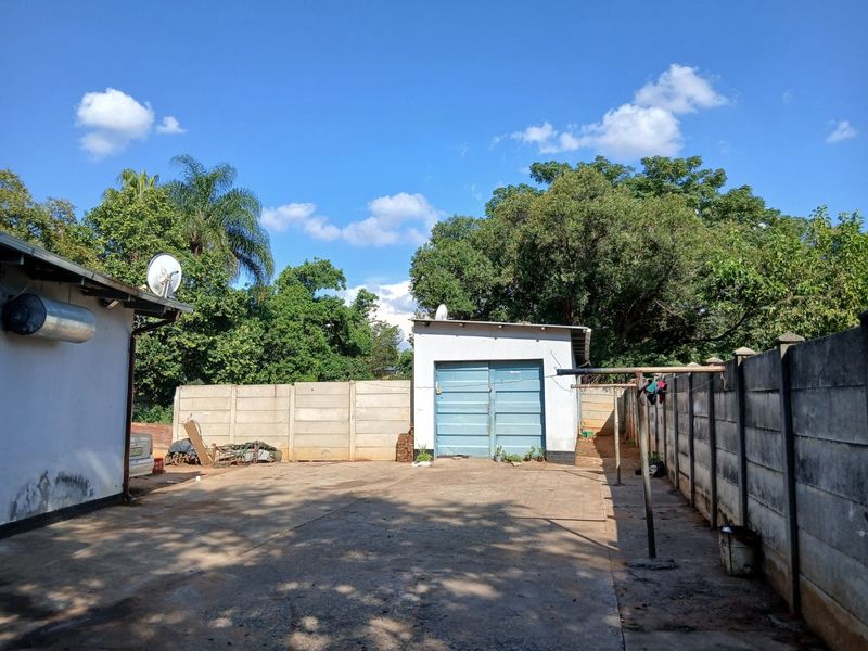 Rear exterior view featuring a concrete driveway, detached garage, and precast concrete boundary walls.