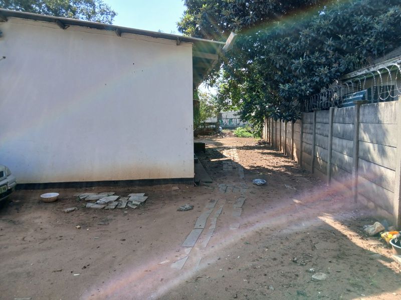 A side or rear exterior view of the property featuring a precast concrete boundary wall with security razor wire and an unpaved ground area.