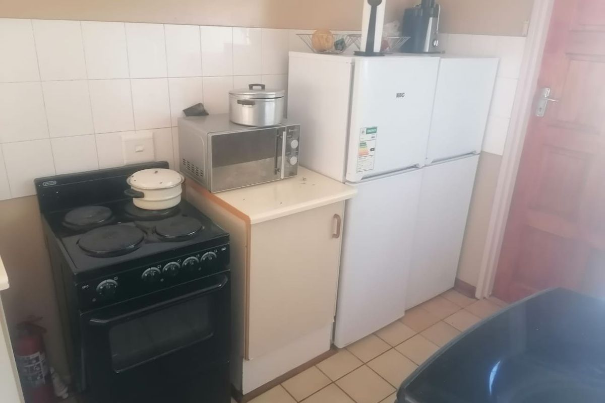 A compact kitchen area featuring a freestanding electric stove, tiled splashback, and basic cabinetry, requiring cosmetic updates to modernize the space.