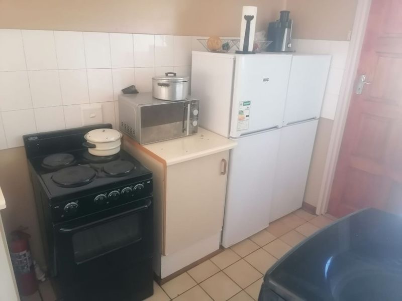A compact kitchen area featuring a freestanding electric stove, tiled splashback, and basic cabinetry, requiring cosmetic updates to modernize the space.
