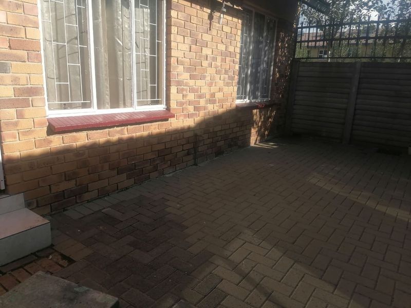 A paved outdoor patio area featuring facebrick walls, security window bars, and a precast concrete boundary wall.