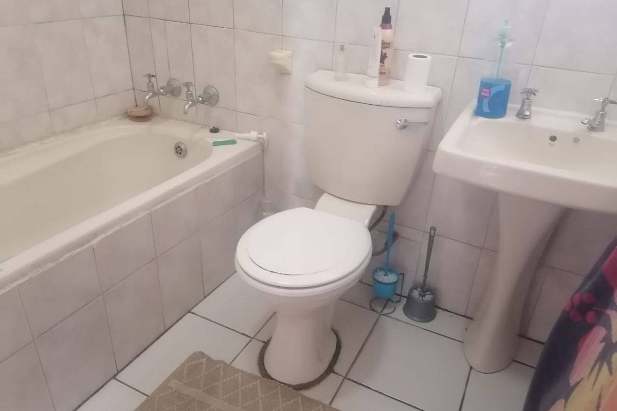 A dated bathroom featuring a standard bathtub, pedestal basin, and toilet with full-height wall tiling and floor tiles.