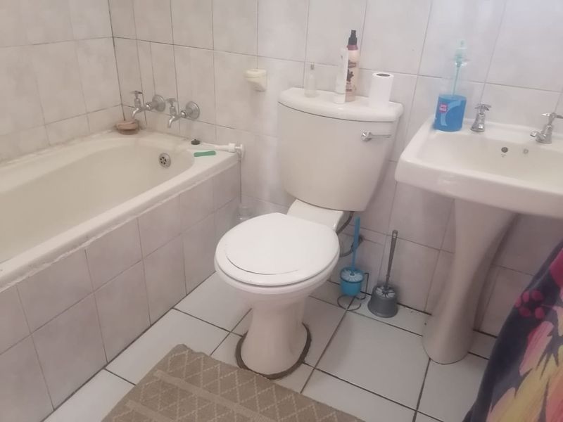 A dated bathroom featuring a standard bathtub, pedestal basin, and toilet with full-height wall tiling and floor tiles.