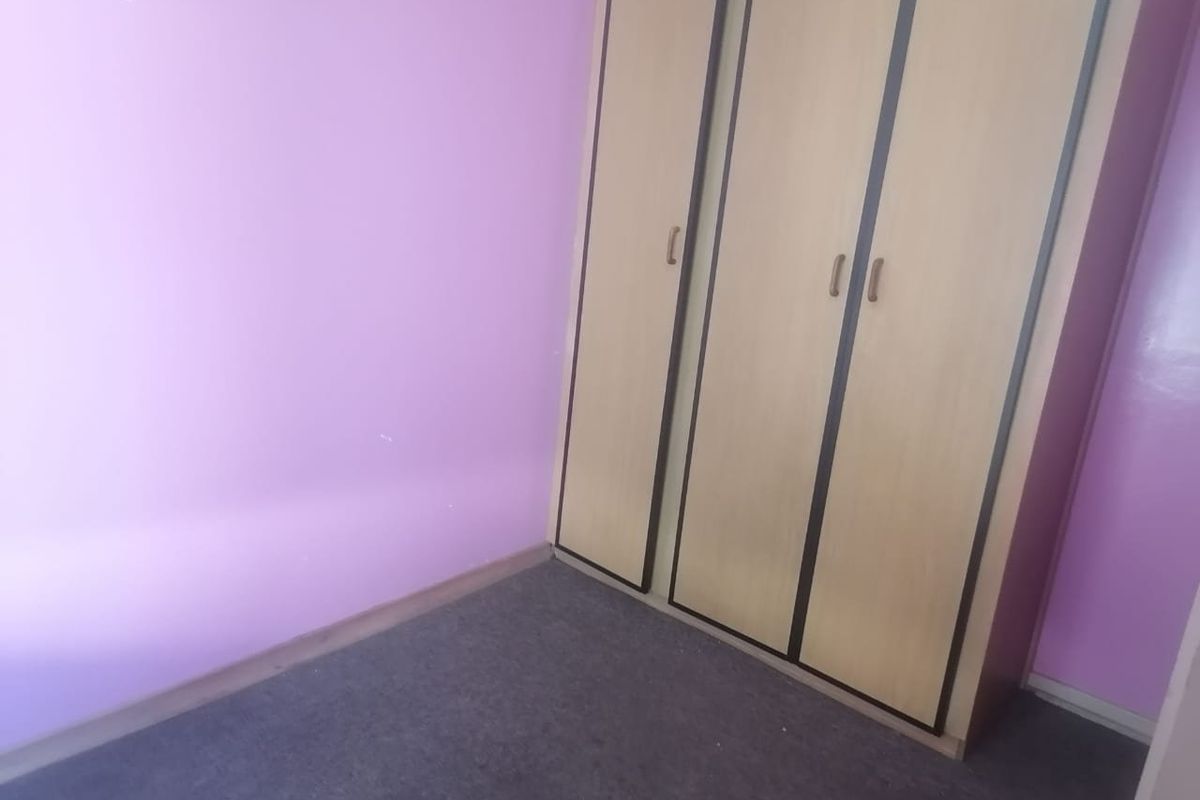 A bedroom featuring a built-in wardrobe, purple painted walls, and carpeted flooring. The space is vacant and ready for renovation or restyling.