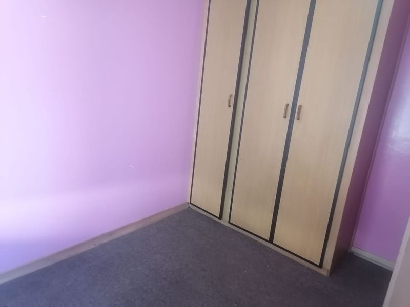 A bedroom featuring a built-in wardrobe, purple painted walls, and carpeted flooring. The space is vacant and ready for renovation or restyling.