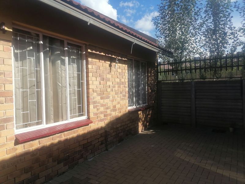 A rear exterior view of a townhouse featuring a face brick facade, paved courtyard area, and secure perimeter fencing.