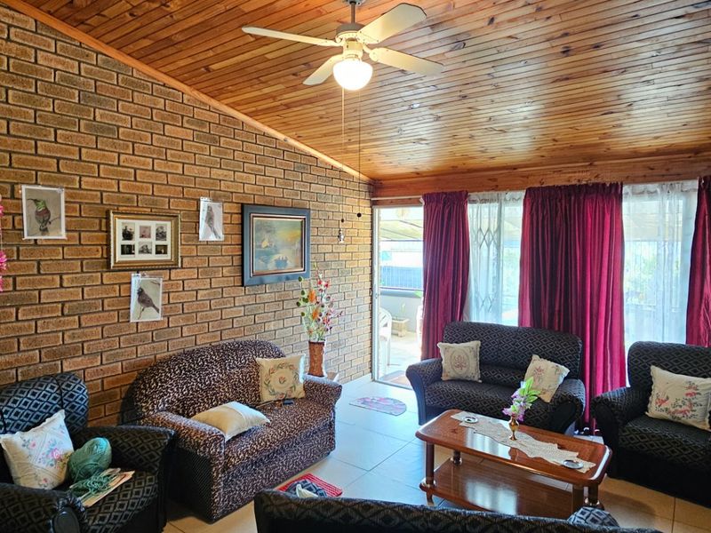 A living room featuring an exposed brick wall, timber ceiling, and tiled flooring, with direct access to an outdoor area through a sliding glass door.