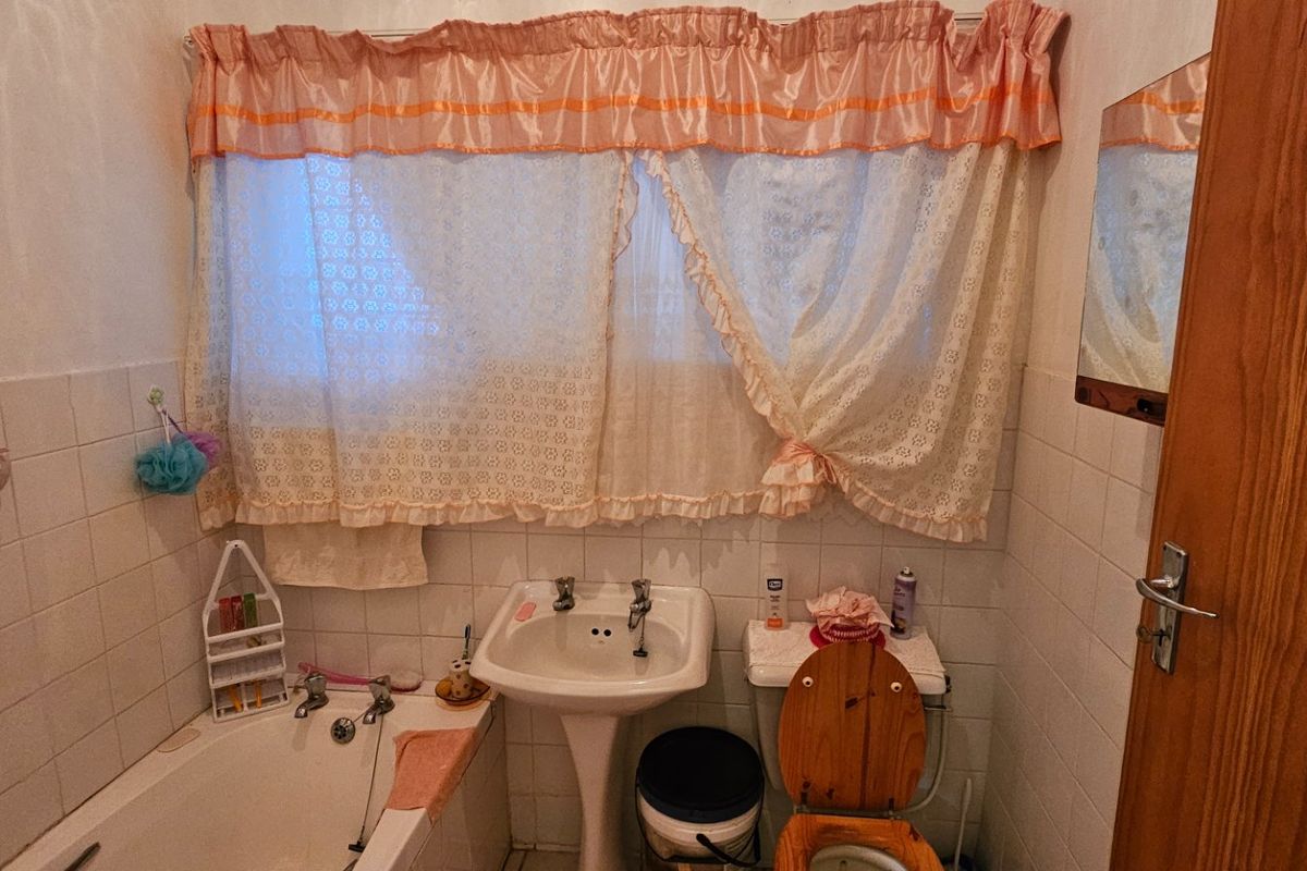 A compact bathroom featuring a pedestal basin, bathtub, and toilet with classic wall tiling, offering potential for a modern renovation.