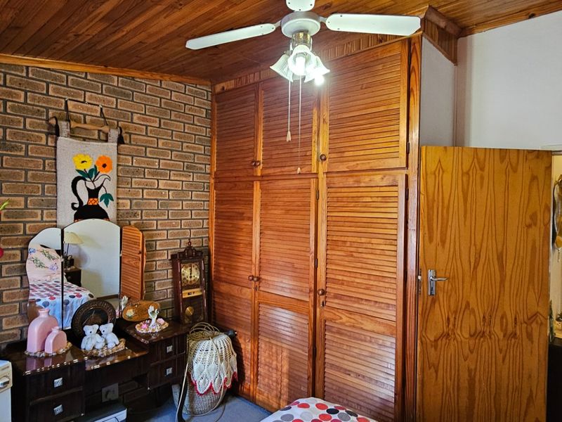 Bedroom featuring exposed brickwork, timber ceiling, and extensive built-in wooden cabinetry with louvered doors.