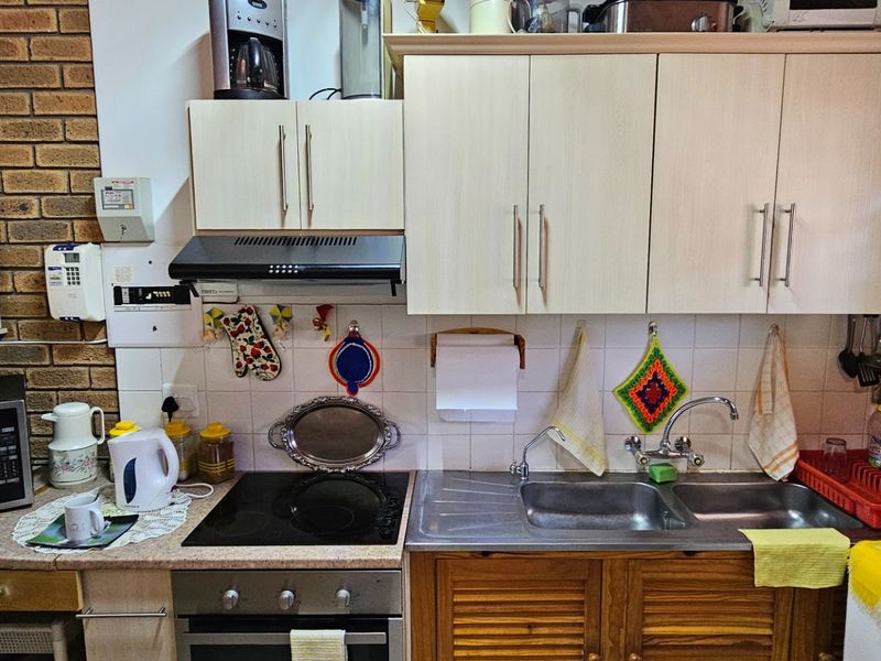 A functional kitchen featuring laminate cabinetry, an electric hob with extractor fan, built-in oven, and a double bowl stainless steel sink with tiled splashback.