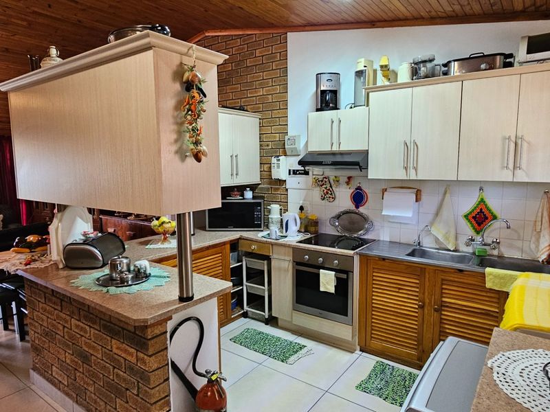 Open plan kitchen and living area featuring timber ceilings, exposed brick accents, and functional cabinetry with integrated cooking appliances.