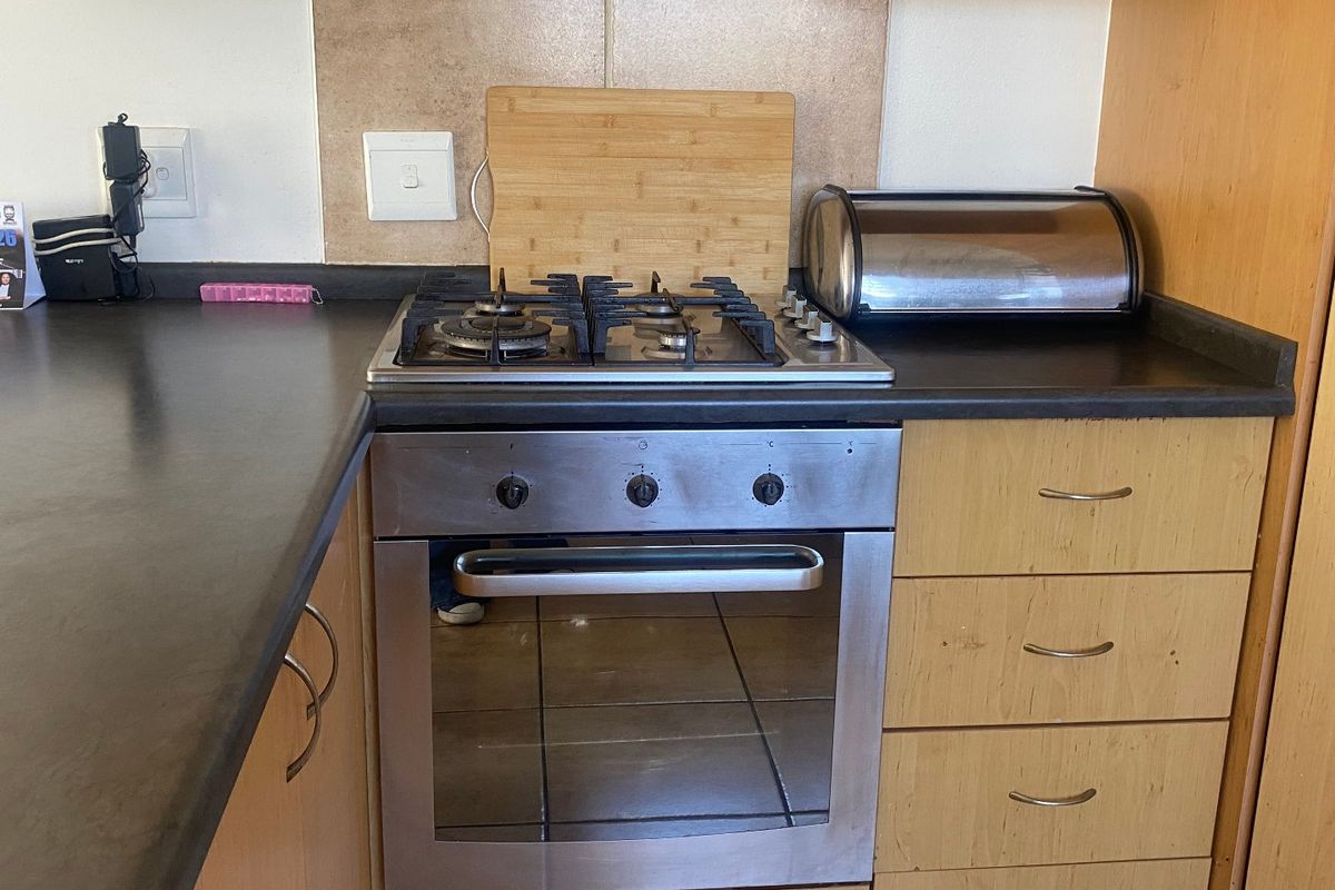 A functional kitchen area featuring a built-in gas hob, oven, laminate cabinetry, and a tiled backsplash, providing a practical workspace.