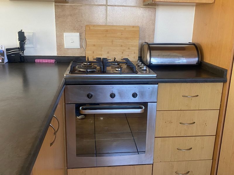 A functional kitchen area featuring a built-in gas hob, oven, laminate cabinetry, and a tiled backsplash, providing a practical workspace.