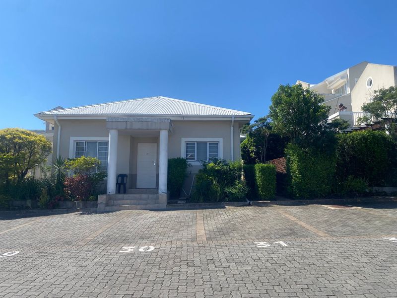 Front elevation of a townhouse featuring a paved driveway, covered entrance porch with concrete columns, and a metal roof.