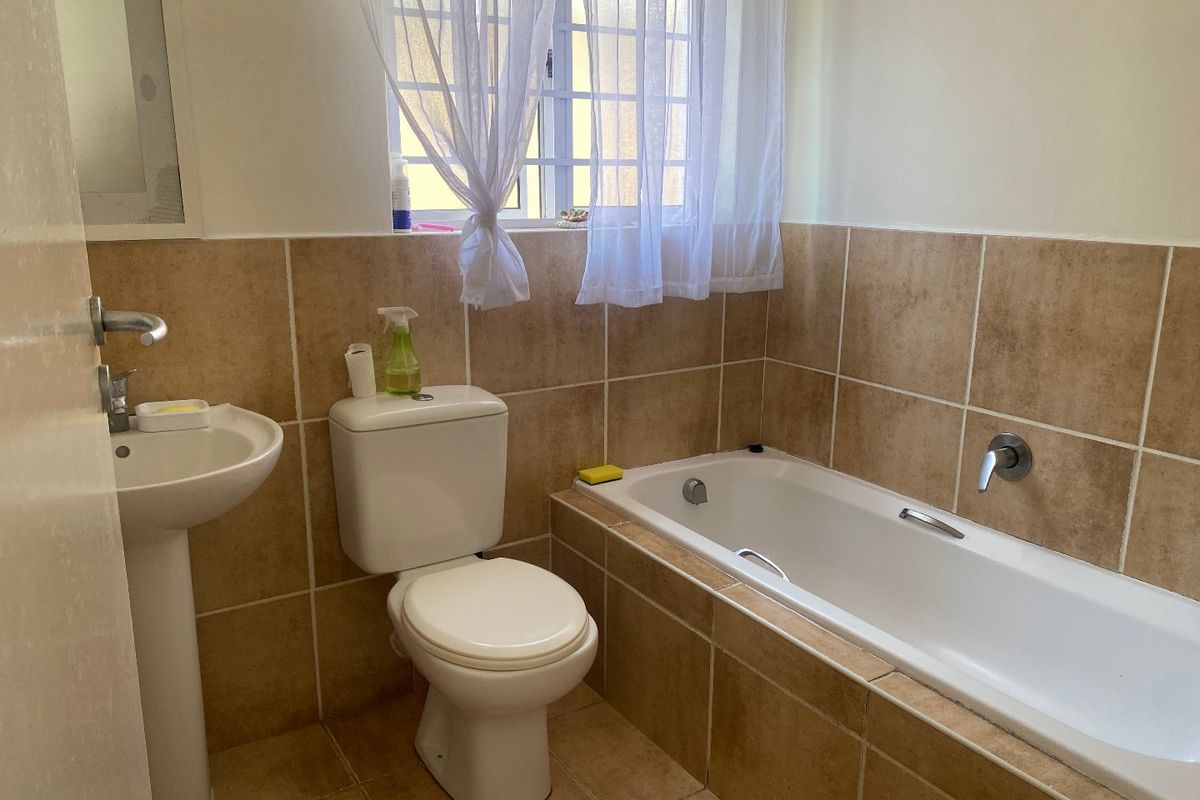 A functional bathroom featuring a pedestal basin, toilet, and a built-in bathtub with neutral wall and floor tiling.