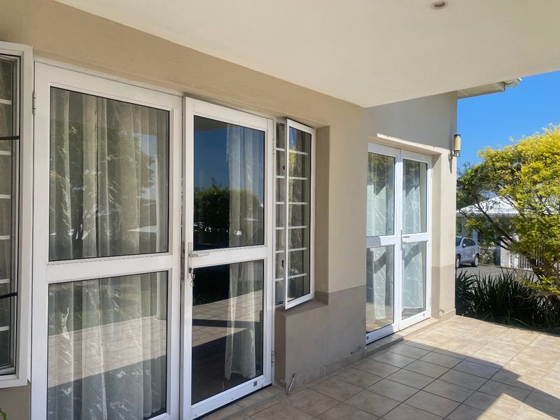 A covered patio area featuring tiled flooring and white aluminium framed glass doors providing access to the interior living space.