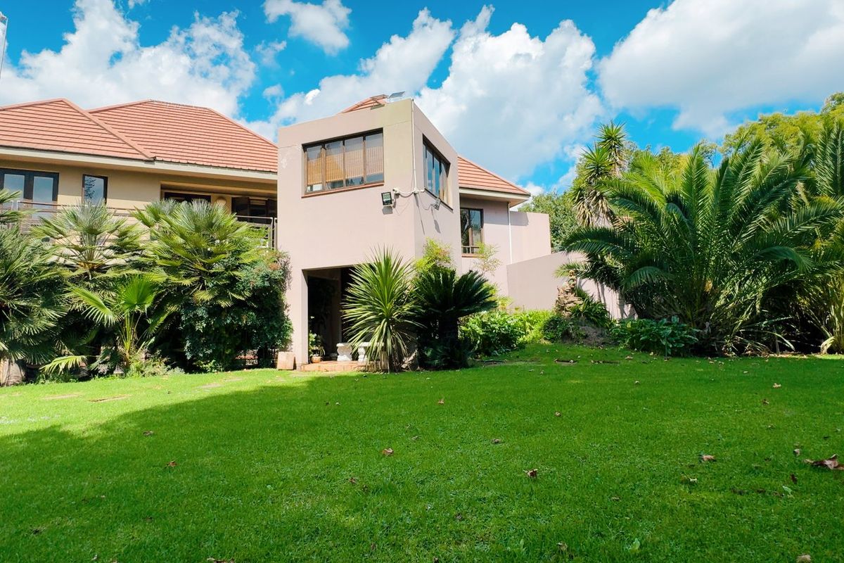 Rear view of the property featuring a multi-level facade, tiled roof, balcony, and a well-maintained garden area.