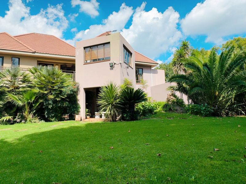 Rear view of the property featuring a multi-level facade, tiled roof, balcony, and a well-maintained garden area.