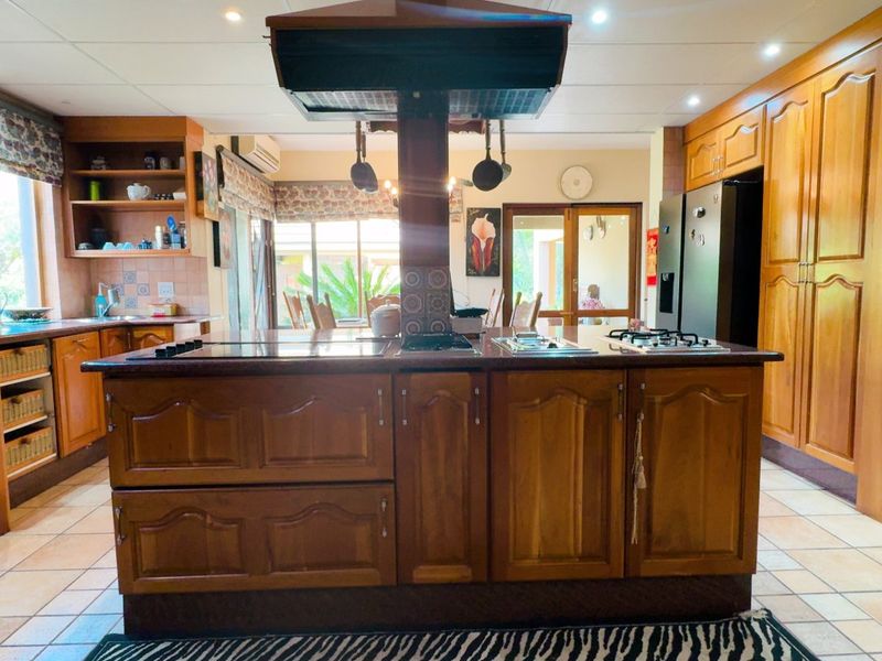 Spacious kitchen featuring extensive wooden cabinetry, a central island with integrated cooktop and extractor fan, and tiled flooring throughout.