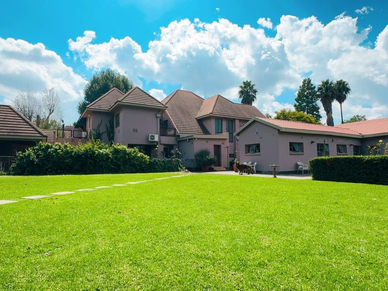 A spacious rear garden view featuring a well-maintained lawn, mature hedges, and the rear elevation of the house with a tiled roof.