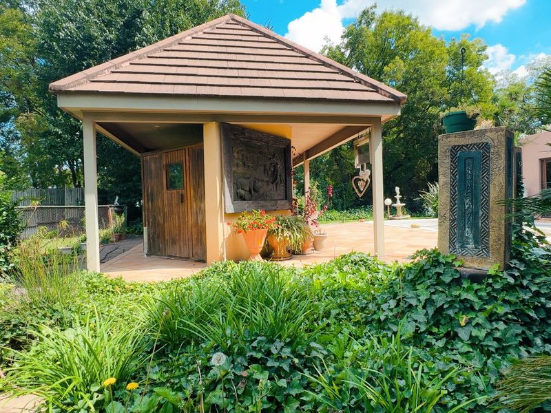 A covered outdoor patio area featuring tiled flooring, a hipped roof structure, and a decorative stone water feature set within a lush garden.