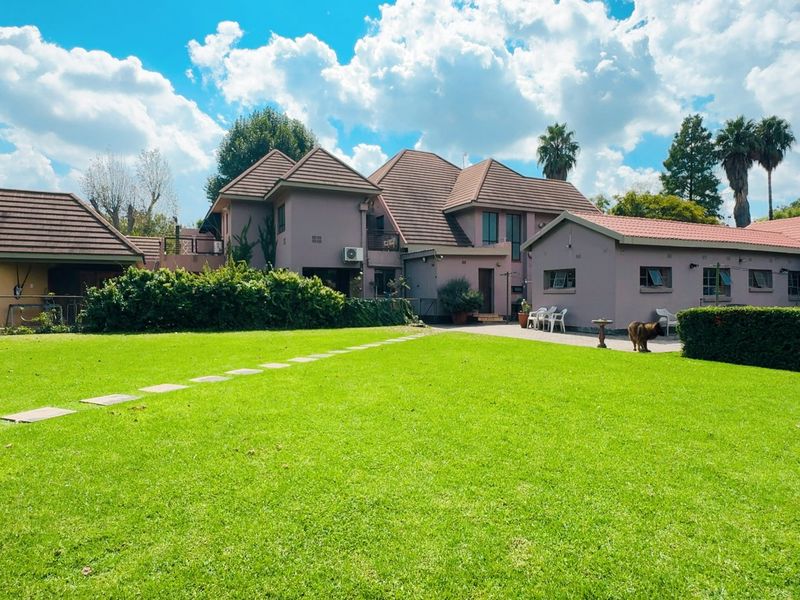 Spacious rear garden view featuring a large manicured lawn, paved pathways, and a covered patio area attached to the main house structure.