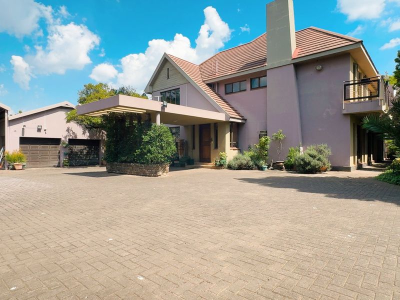 Spacious front exterior view featuring a large paved driveway, covered entrance portico, and a multi-level residential structure with a tiled roof.
