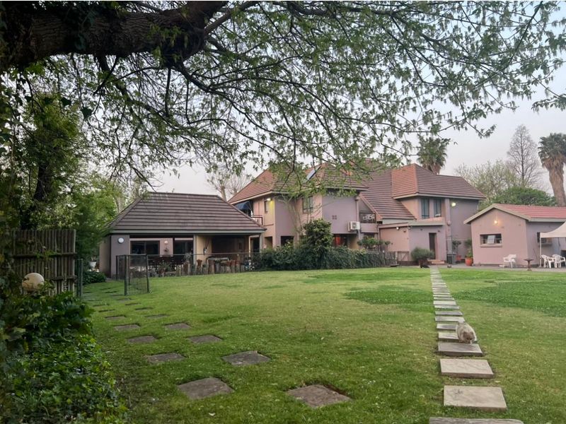 A spacious rear garden featuring a well-maintained lawn, stone pathways, and a view of the multi-level residential building with a tiled roof.