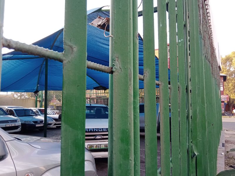View of a commercial parking area secured by a green metal fence with an overhead shade cloth structure.