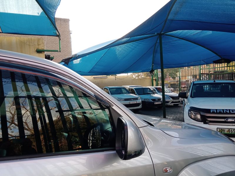 Outdoor commercial parking area featuring a blue shade cloth canopy structure and perimeter security fencing.