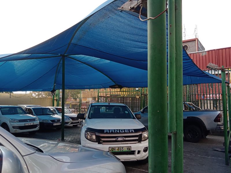 Commercial parking area featuring a large blue shade cloth canopy supported by steel poles over a paved surface.