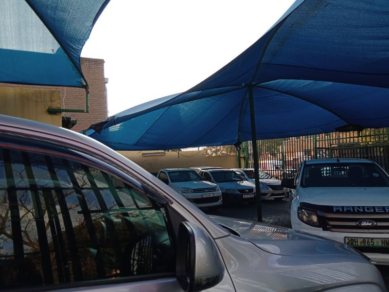 Commercial parking area featuring a large blue shade cloth canopy structure and perimeter security fencing.
