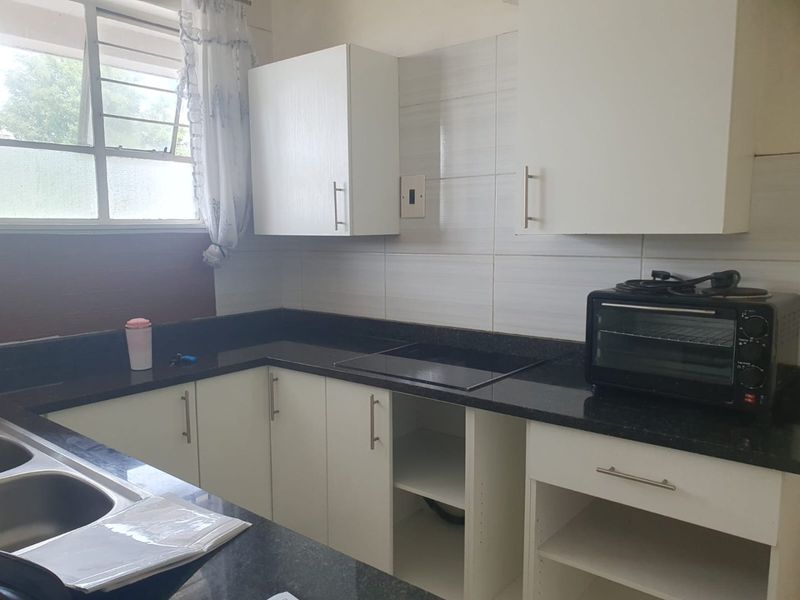 Kitchen featuring white cabinetry, dark granite countertops, a double bowl sink, and a built-in hob, requiring minor repairs to cabinetry.