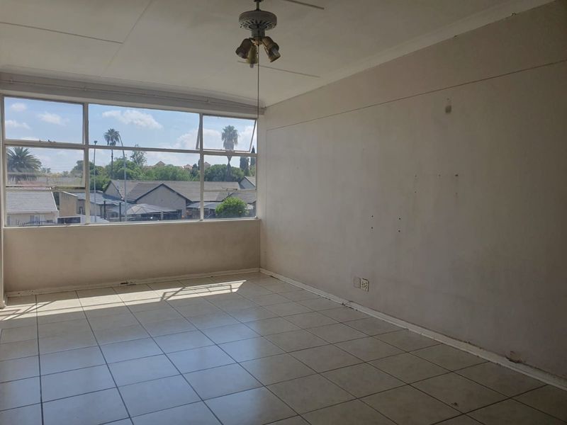 An empty living room featuring tiled flooring, a ceiling fan, and large windows providing natural light and neighborhood views.