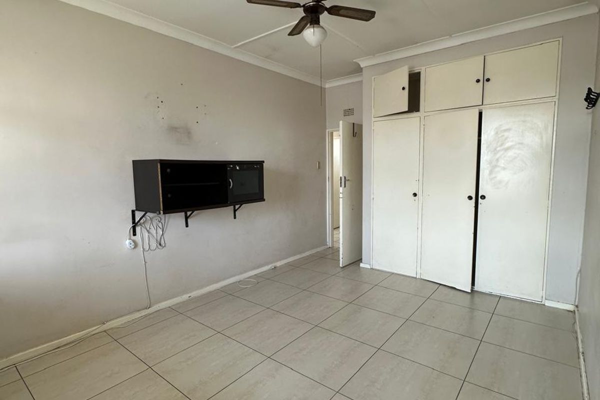 An empty bedroom featuring tiled flooring, a ceiling fan, and built-in storage cupboards with overhead compartments.