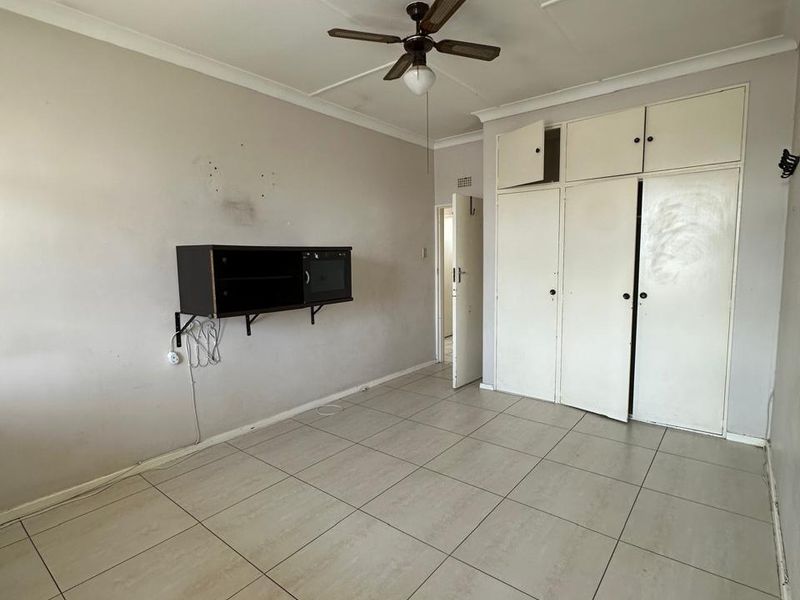 An empty bedroom featuring tiled flooring, a ceiling fan, and built-in storage cupboards with overhead compartments.