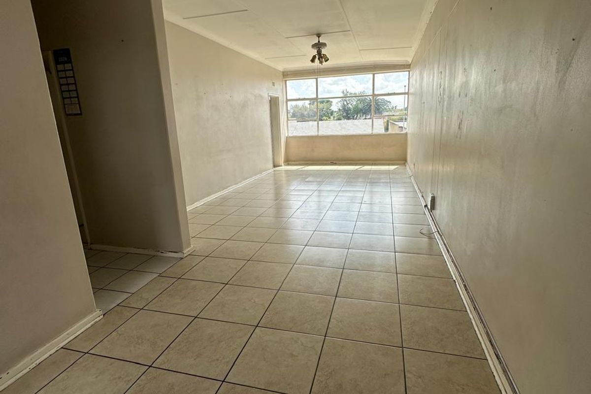 An empty, open-plan living area featuring neutral tiled flooring, a ceiling fan, and large windows providing natural light.